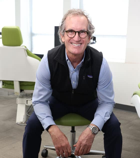 Professional man in glasses seated on green chair in modern office setting, smiling at camera.