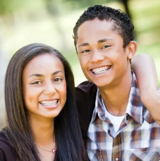 Two smiling teenagers with straight teeth pose together outdoors in natural daylight.