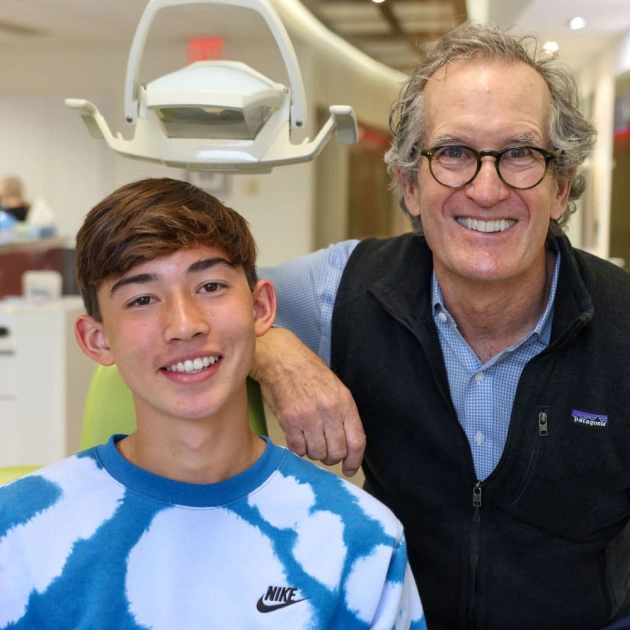 Young patient in blue Nike shirt smiles with orthodontist in dental office setting.